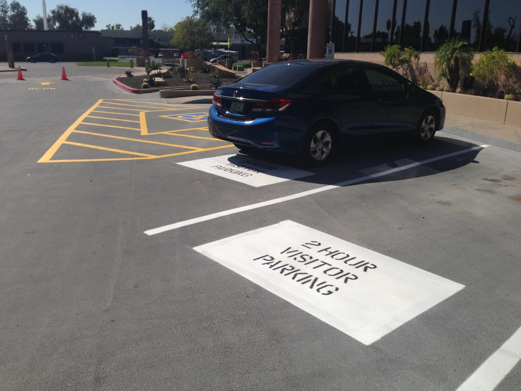 We Do Lines Arizona - A blue car is parked in a parking lot, occupying one of the spaces marked "2 Hour Visitor Parking," its position clearly defined by the fresh line striping.