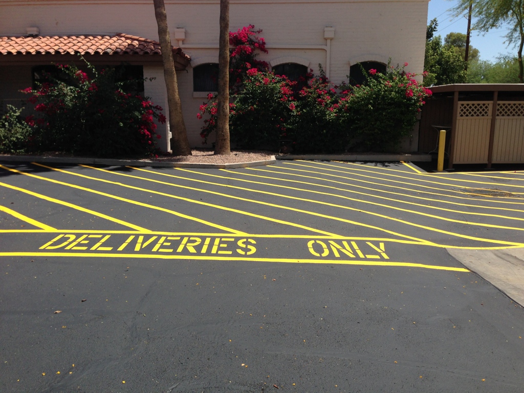 We Do Lines Arizona - Parking lot featuring precise line striping, including a yellow-striped "DELIVERIES ONLY" zone adjacent to a building adorned with red bougainvillaeas and other greenery.