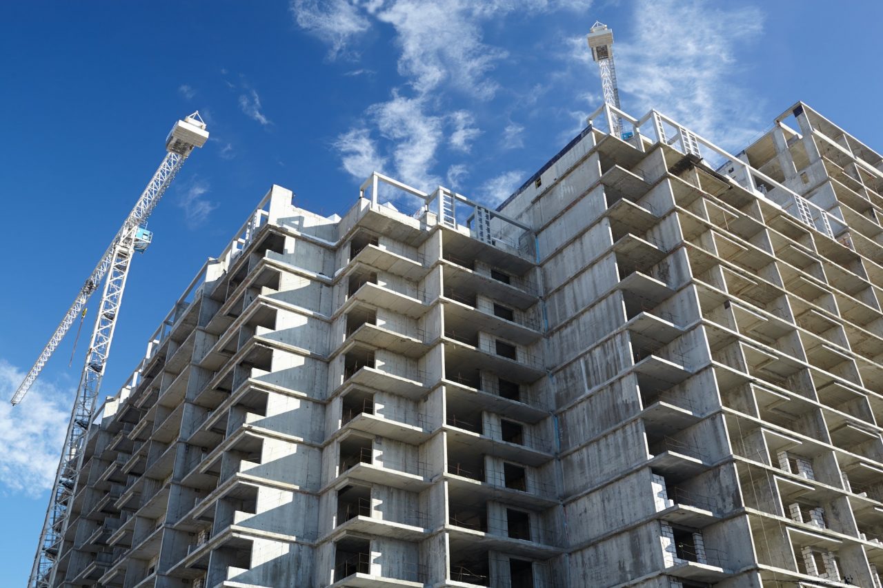 We Do Lines Arizona - A partially constructed concrete building with multiple floors, surrounded by cranes and line striping equipment, under a blue sky with scattered clouds.