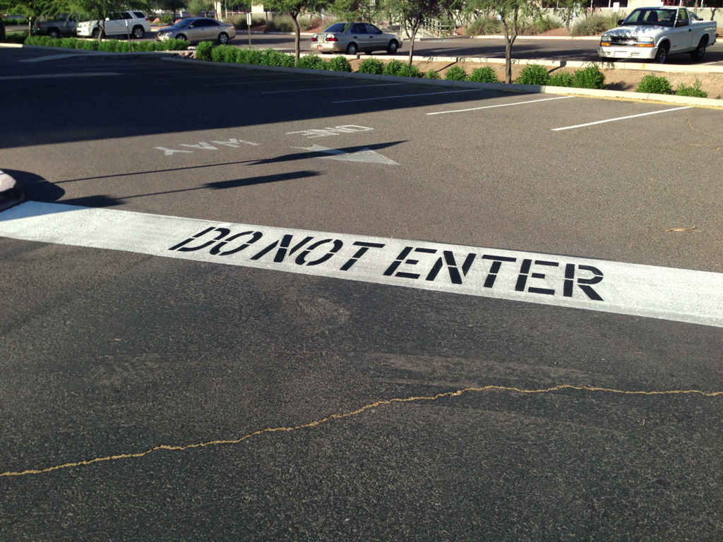 We Do Lines Arizona - A parking lot with a "DO NOT ENTER" sign painted on the asphalt in bold black letters on a white rectangular background. The line striping guides vehicles efficiently, and cars are visible in the background.