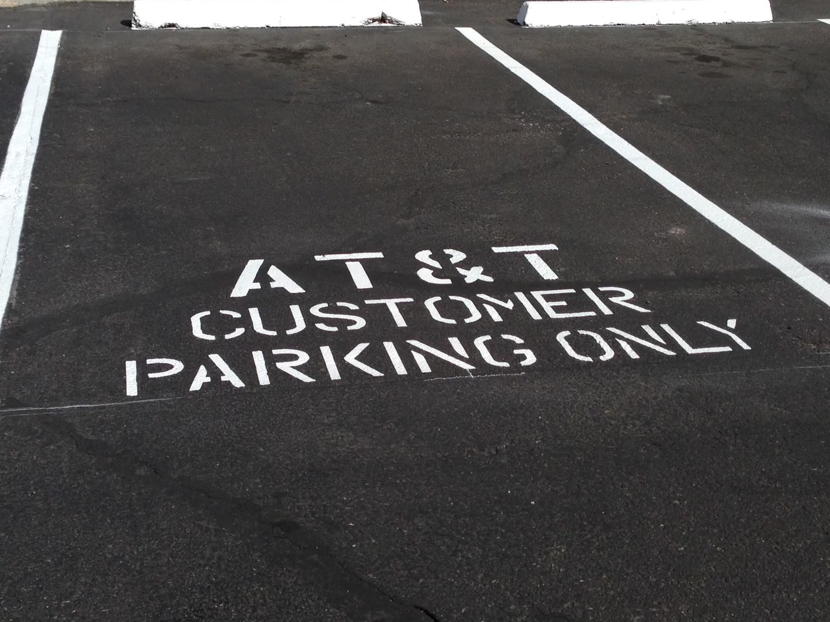 We Do Lines Arizona - A parking space marked with "AT&T Customer Parking Only" in white paint on an asphalt surface, bordered by white line striping and concrete stops.