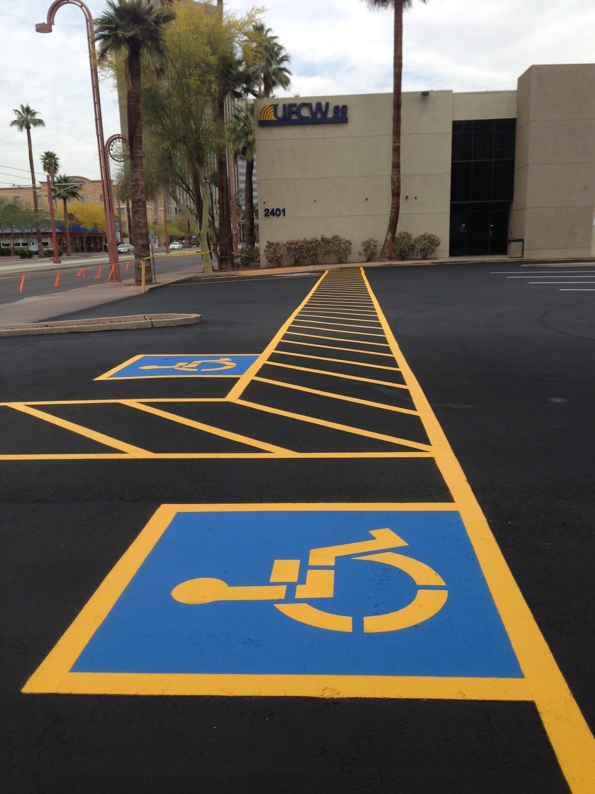 We Do Lines Arizona - A freshly painted parking lot with crisp line striping, featuring two accessible parking spaces marked in blue and yellow lines, located near a building with the sign "UFCW 99" and an address number "2401".