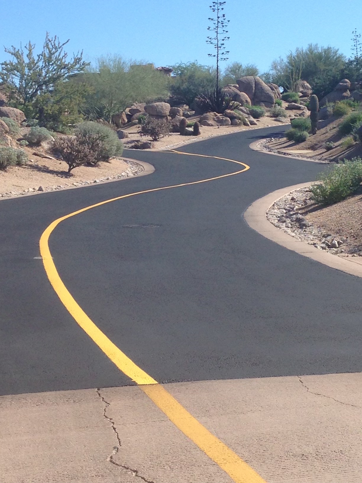 We Do Lines Arizona - A freshly paved road with meticulous line striping curves through a desert landscape featuring rocks, cacti, and other desert vegetation.