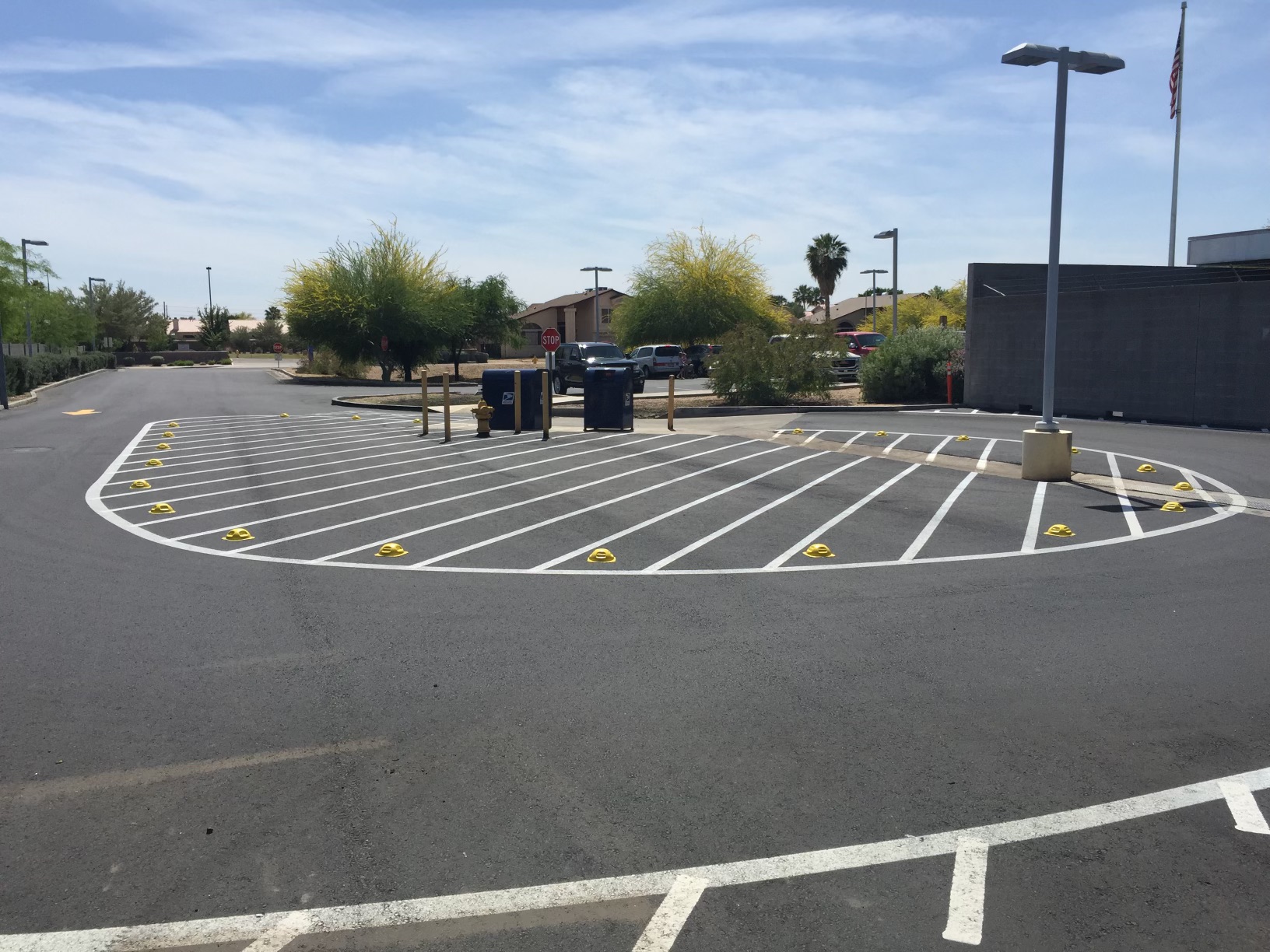 We Do Lines Arizona - A parking lot with numerous parking spaces marked by expert line striping and yellow bumpers, equipped with two blue postal drop boxes under a clear sky.