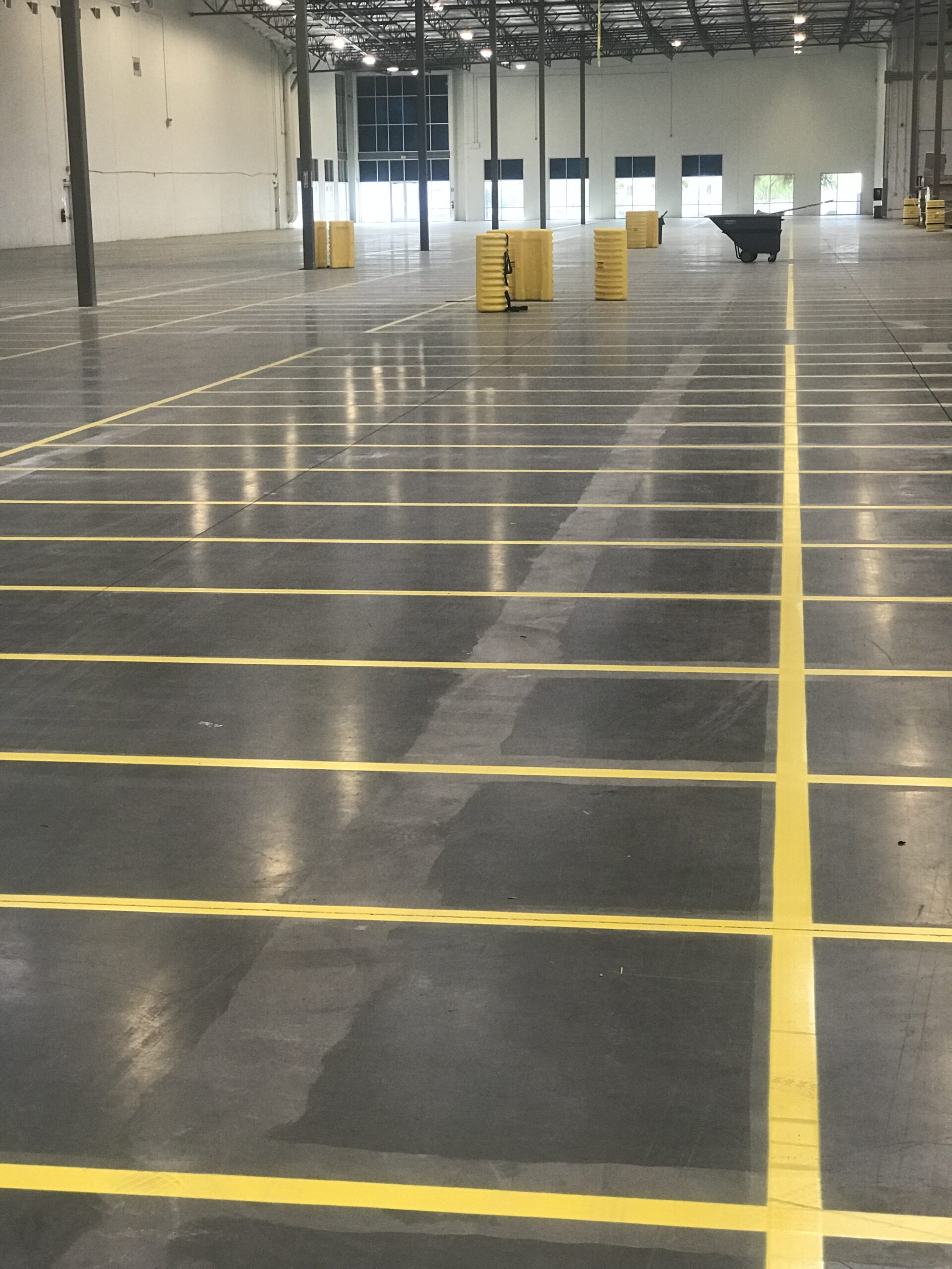 We Do Lines Arizona - An empty warehouse with precise line striping on the floor and several yellow barrels placed in a row at the back.