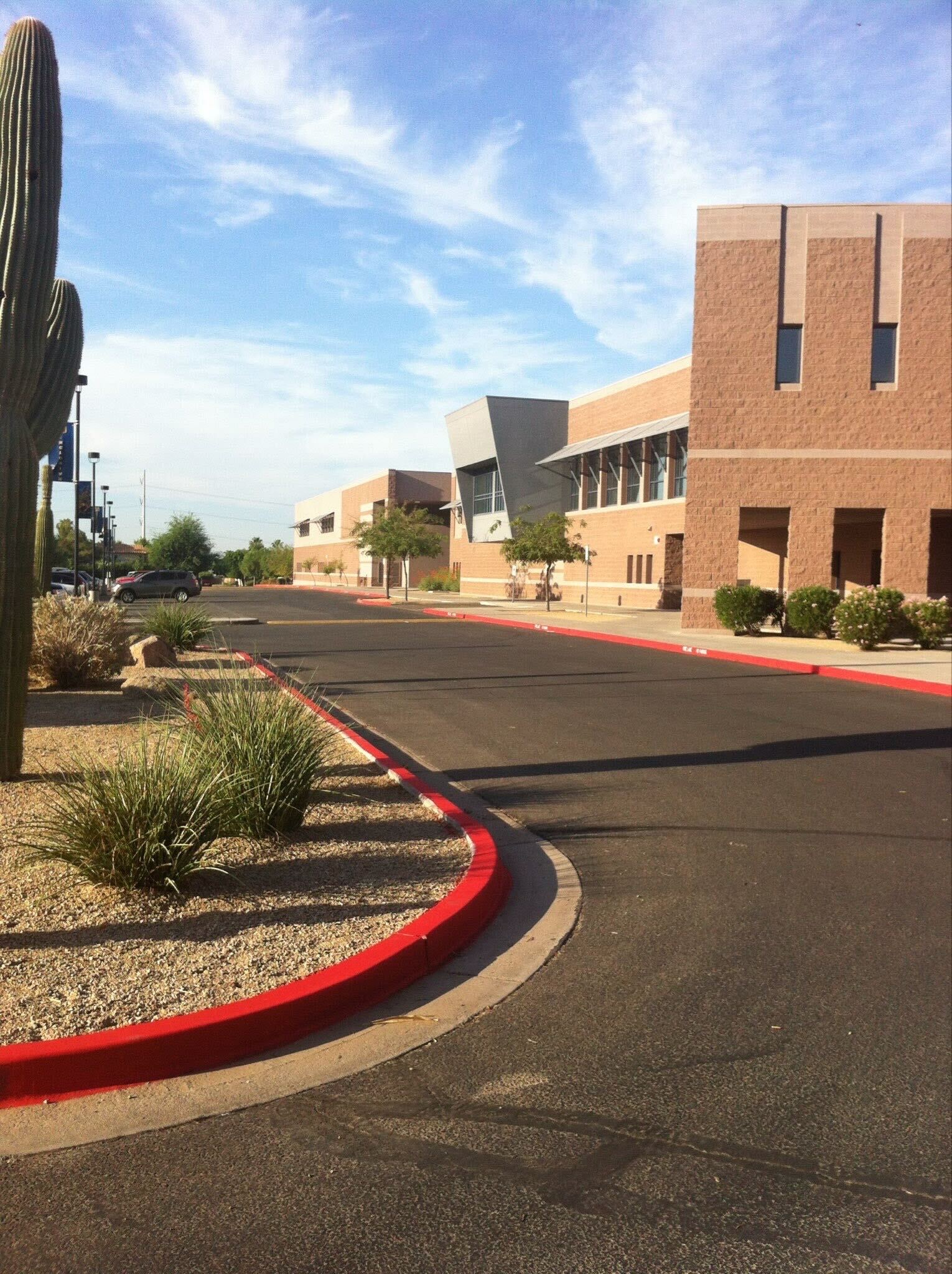 We Do Lines Arizona - A modern brick building with large windows and desert landscaping, including cacti and shrubs, sits adjacent to a wide asphalt road with fresh line striping and a red curb under a clear sky.