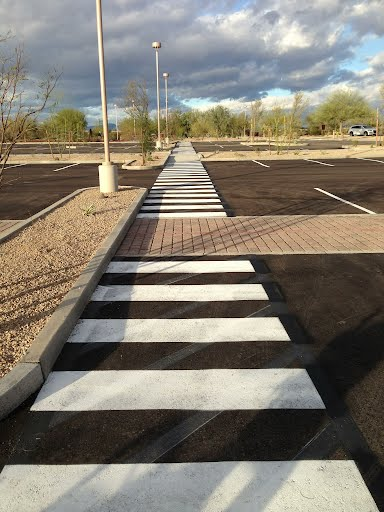 We Do Lines Arizona - A long, striped pedestrian crosswalk with impeccable line striping extends through a parking lot with a mix of asphalt, gravel, and cobblestone under a partly cloudy sky.